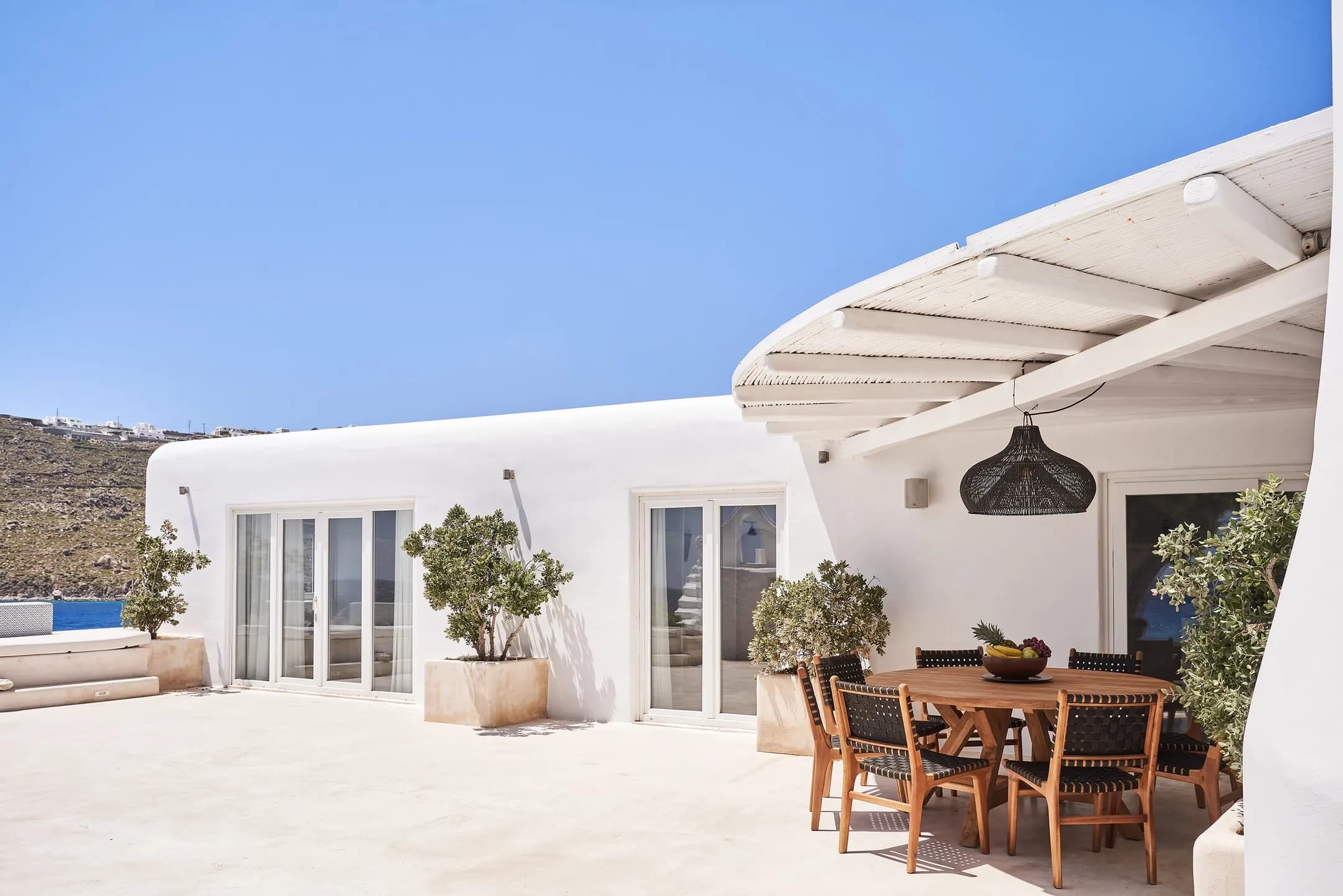 Whitewashed villa exterior with a shaded terrace dining table and potted plants