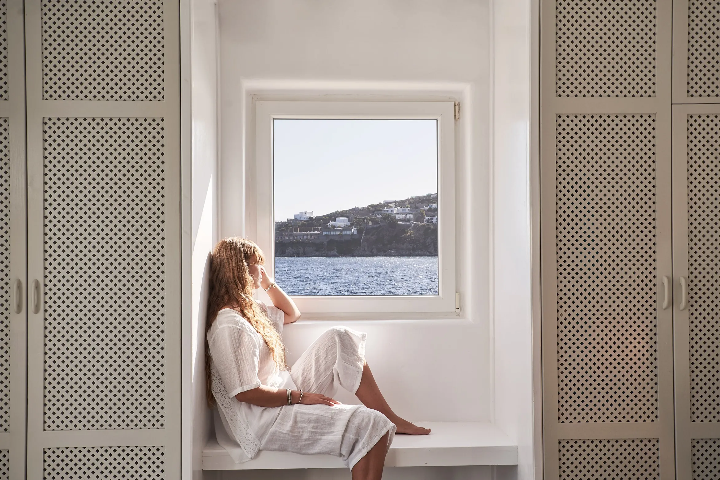 Guest sitting in a bedroom window seat with a view of the sea