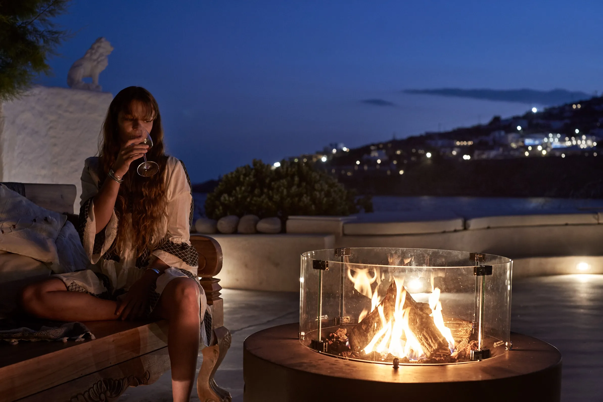 Guest with a glass of wine beside the outdoor fire pit at Santa Katerina by night
