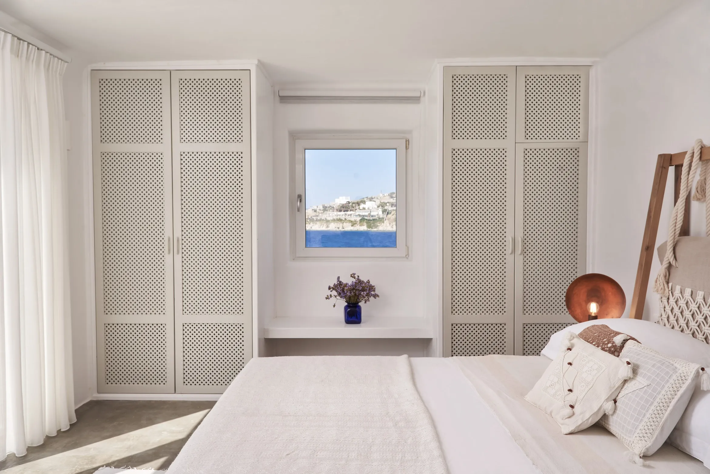 White bedroom with latticed wardrobes, a double bed and a small sea-view window