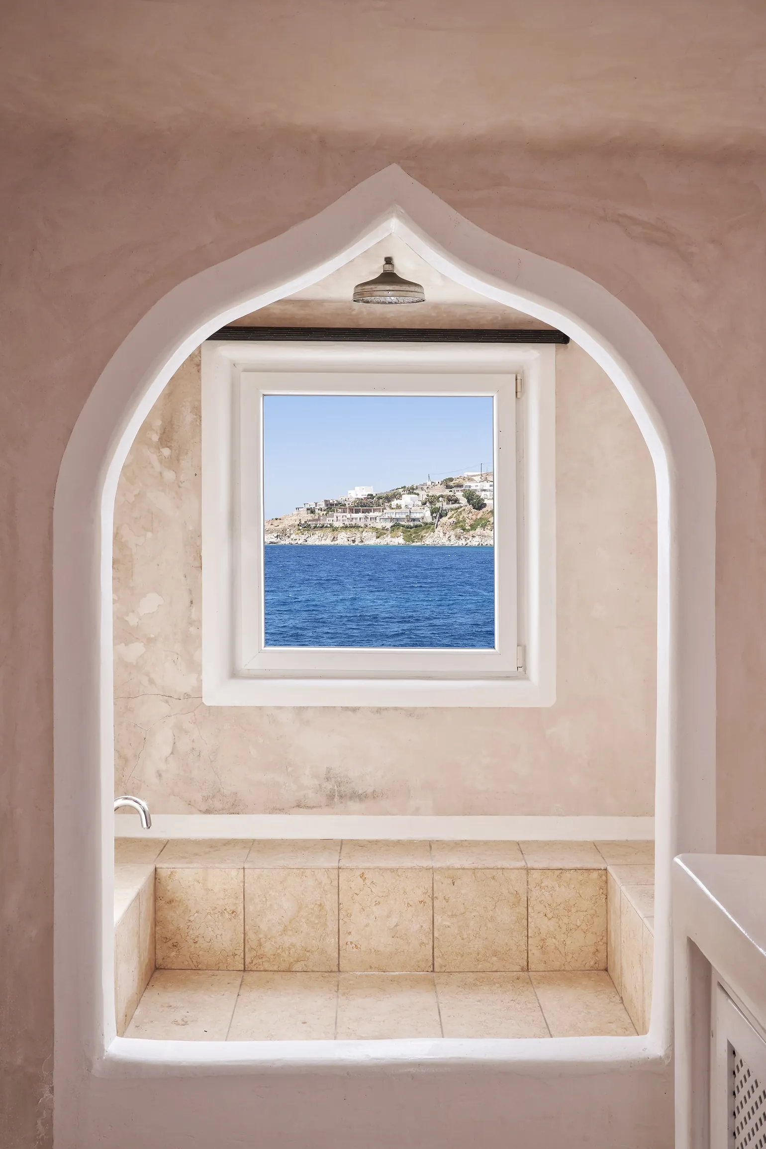 Arched window niche framing the sea and the hillside across the bay